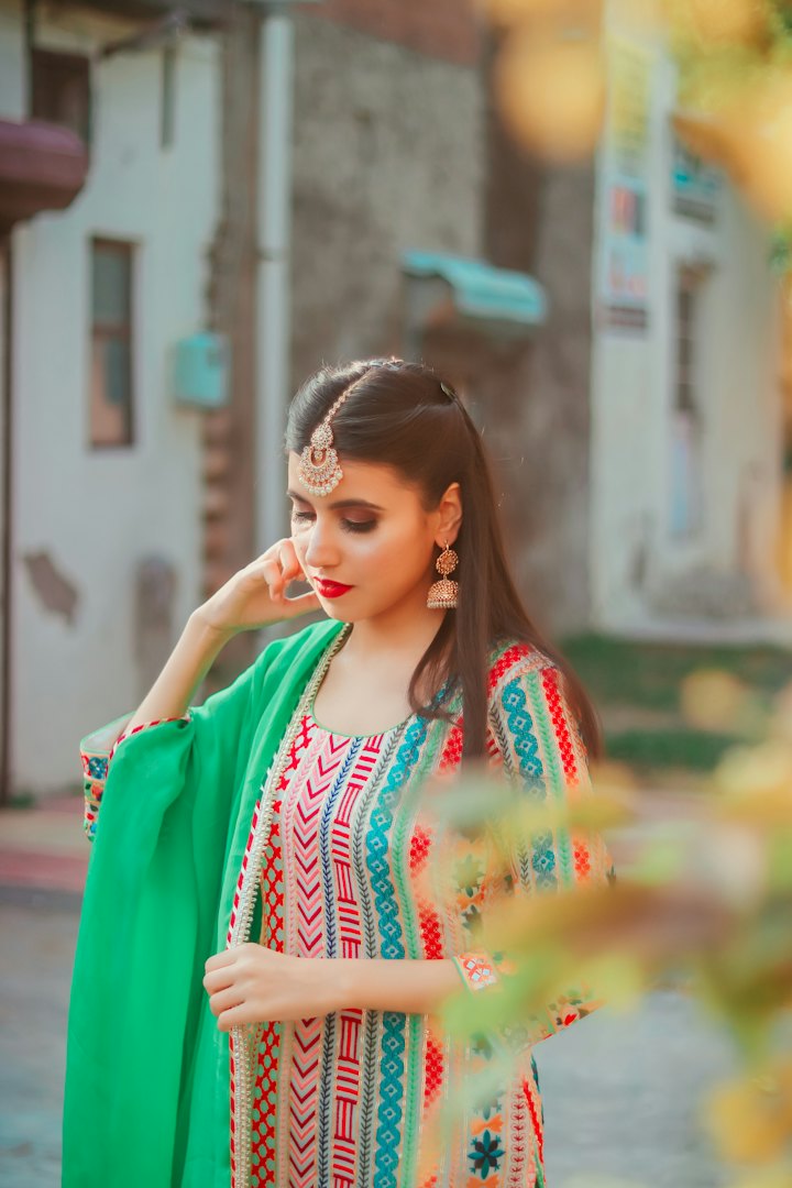 A woman in a green embroidered outfit with a maang tikka and earrings