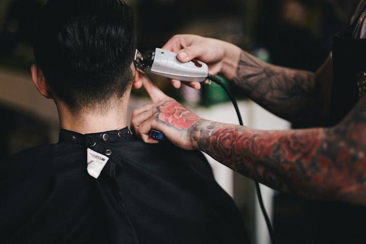 A barber uses clippers on the back of a client's head