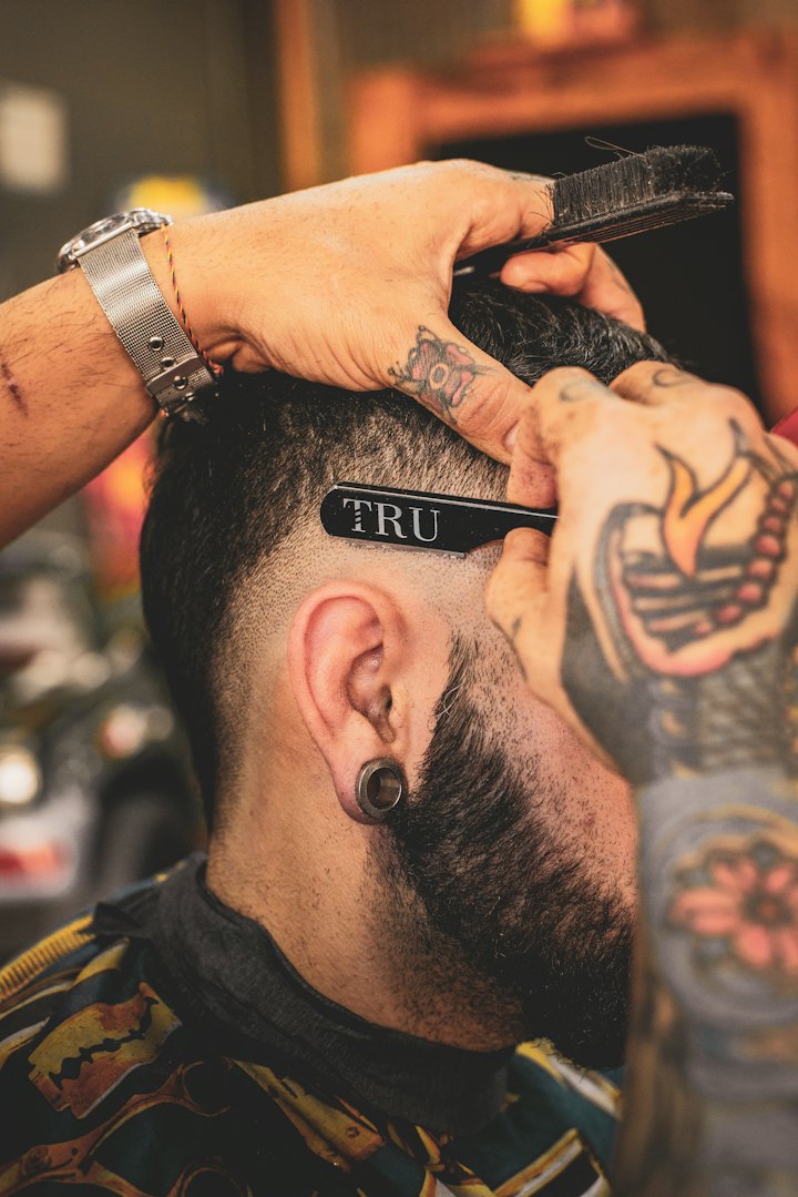A barber combs a client's sharply shaped beard and fade