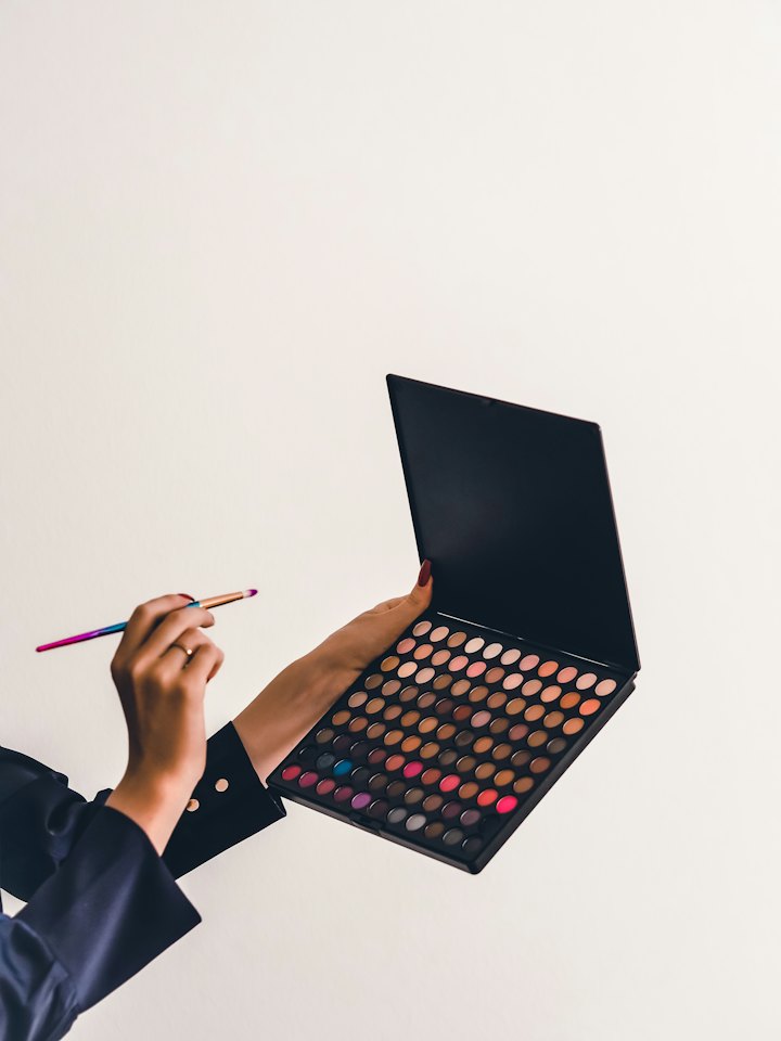 A makeup artist holds an eyeshadow palette and brush