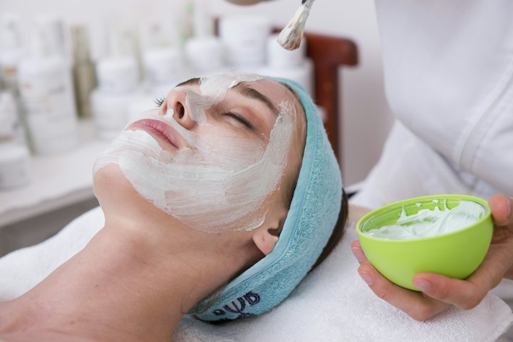 A client with a hair band receives a cream facial mask