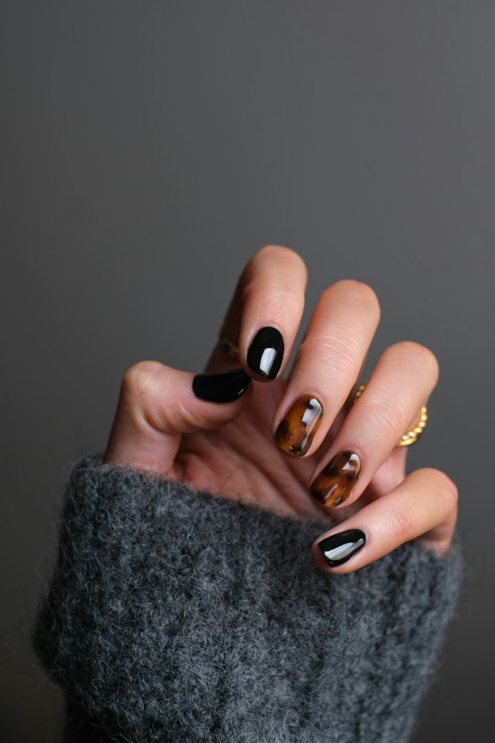 A hand with glossy dark tortoiseshell nail art against a grey sweater