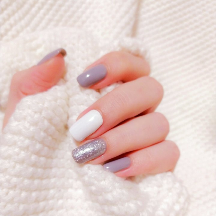 A hand with lilac, white and silver manicured nails on a knitted throw