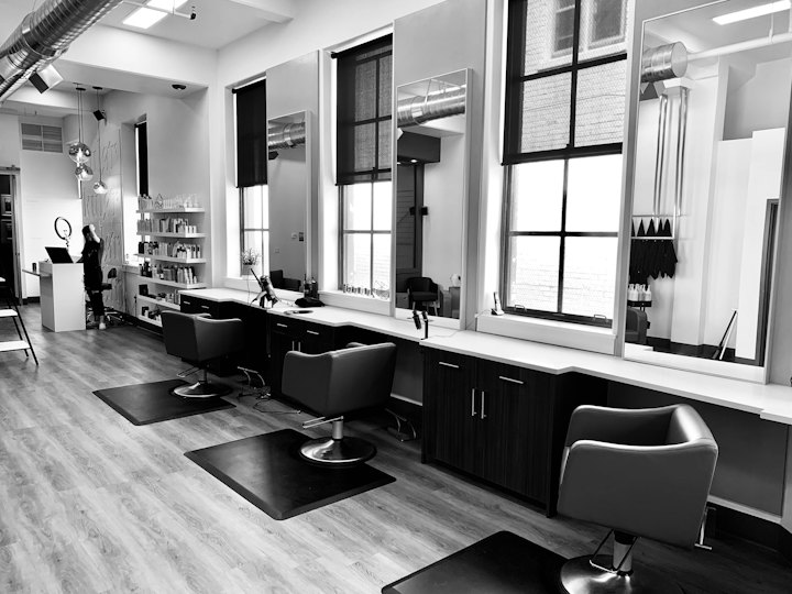 A row of styling stations with large windows and black chairs
