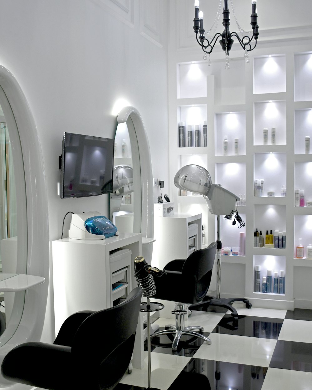 A bright white studio interior with arched mirrors, shelving and a chandelier