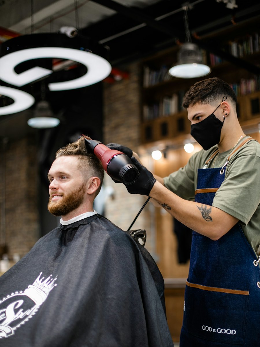A groomer styles a smiling man's hair with a blow-dryer in a barber chair