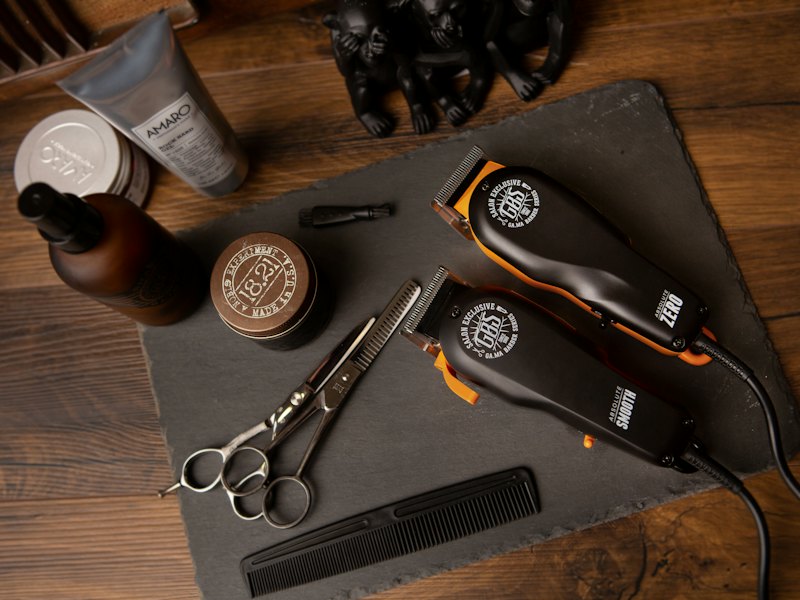 Clippers, scissors, combs and grooming products laid out on a dark wooden surface