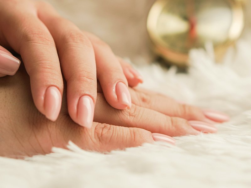 Hands with a neat nude manicure resting on a soft white throw