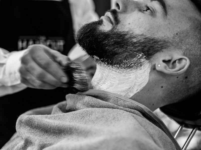 Black-and-white close-up of a lather brush on a man's beard and cheek