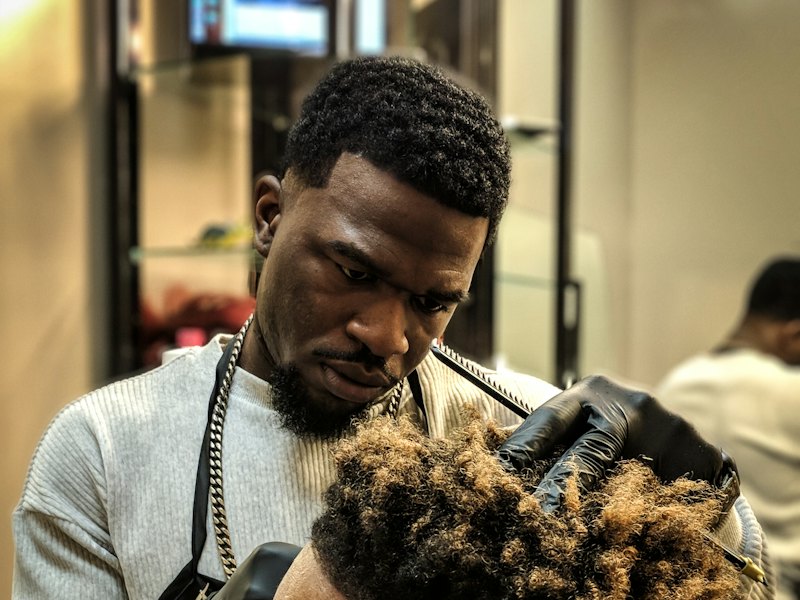 A barber shapes a client's textured curls with a precise fade