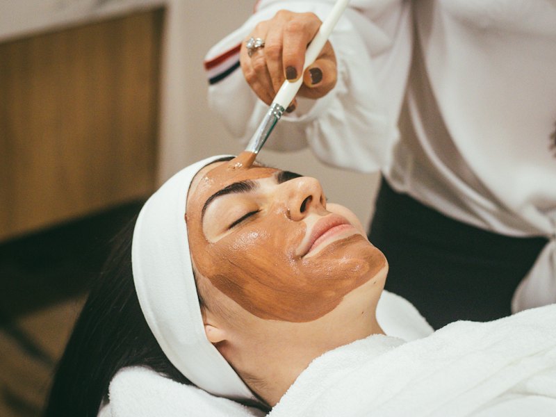 A face mask is applied with a brush to a relaxed client