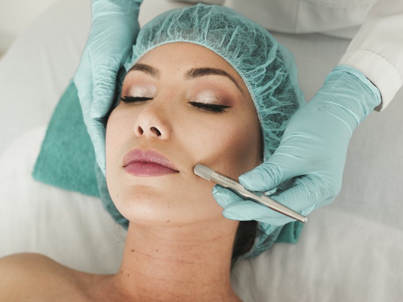 A gloved specialist examines a relaxed client's skin during a facial