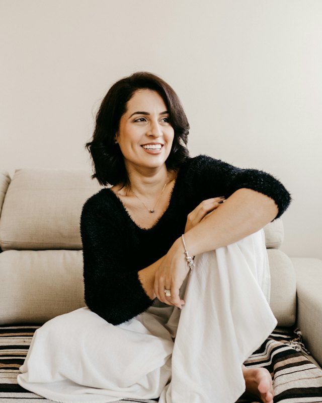 Portrait of a smiling woman with shoulder-length dark hair in a black top (stock photo for the fictional profile of Priya)